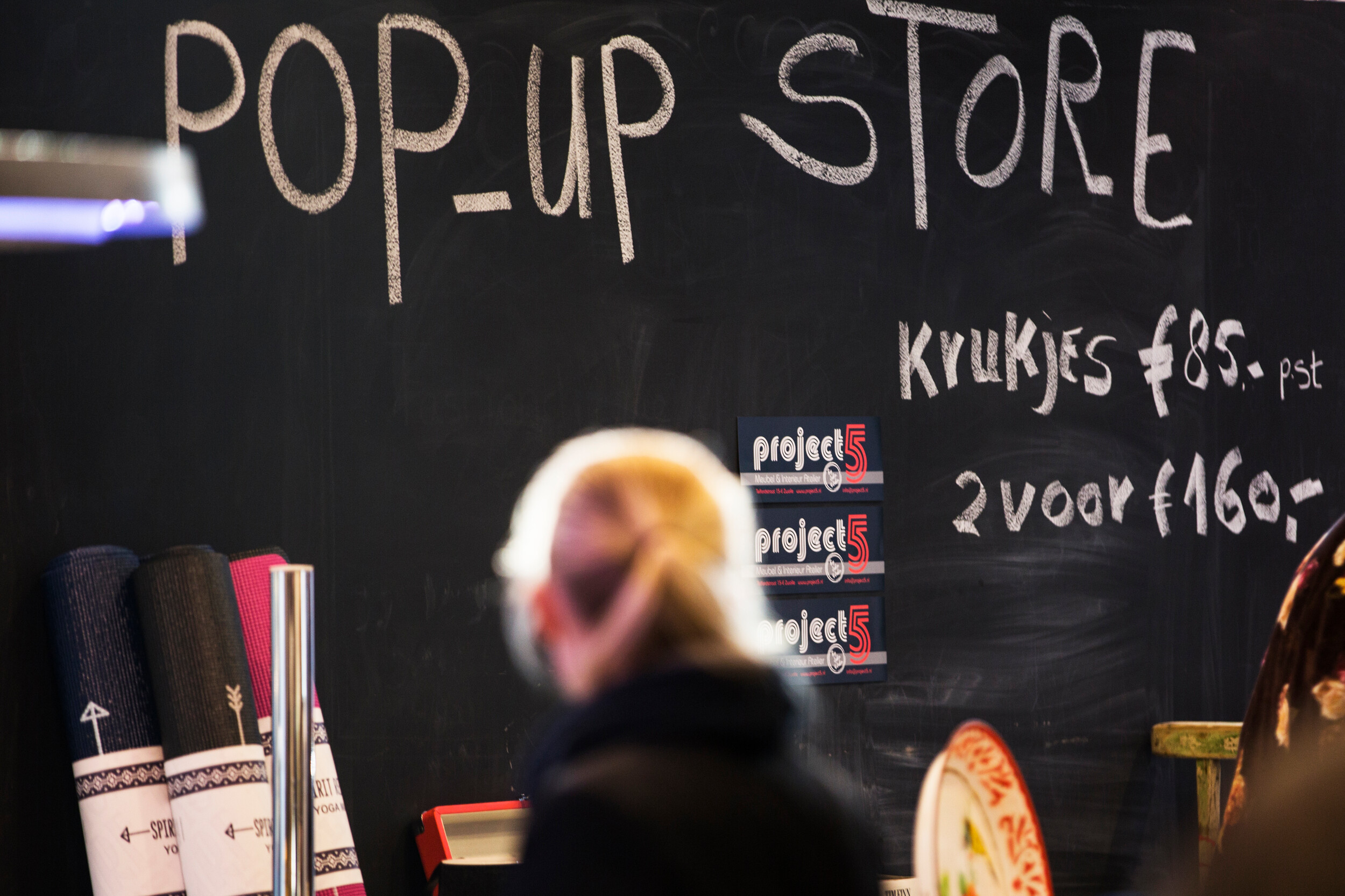 Sfeerbeeld van iemand voor krijtbord met daarop: "Pop up store en krukjes voor 85 euro en 2 voor 160 euro" 