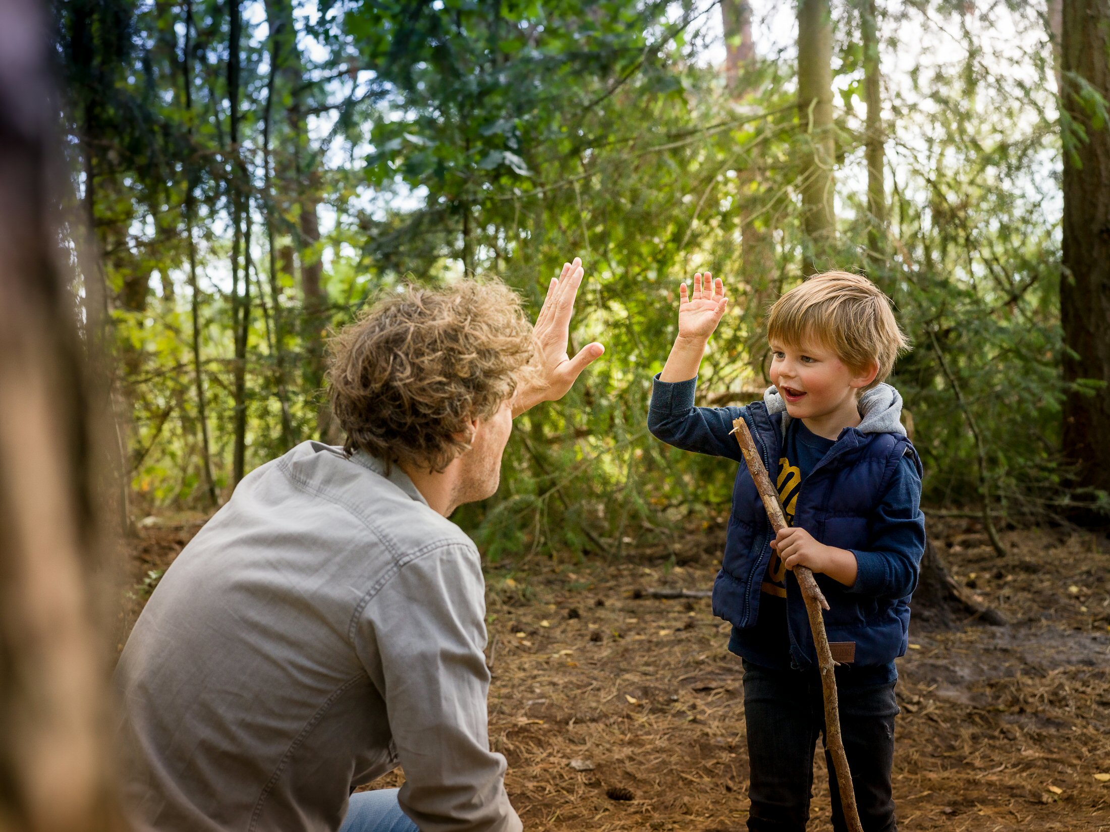 kind geeft iemand high five tussen de bomen