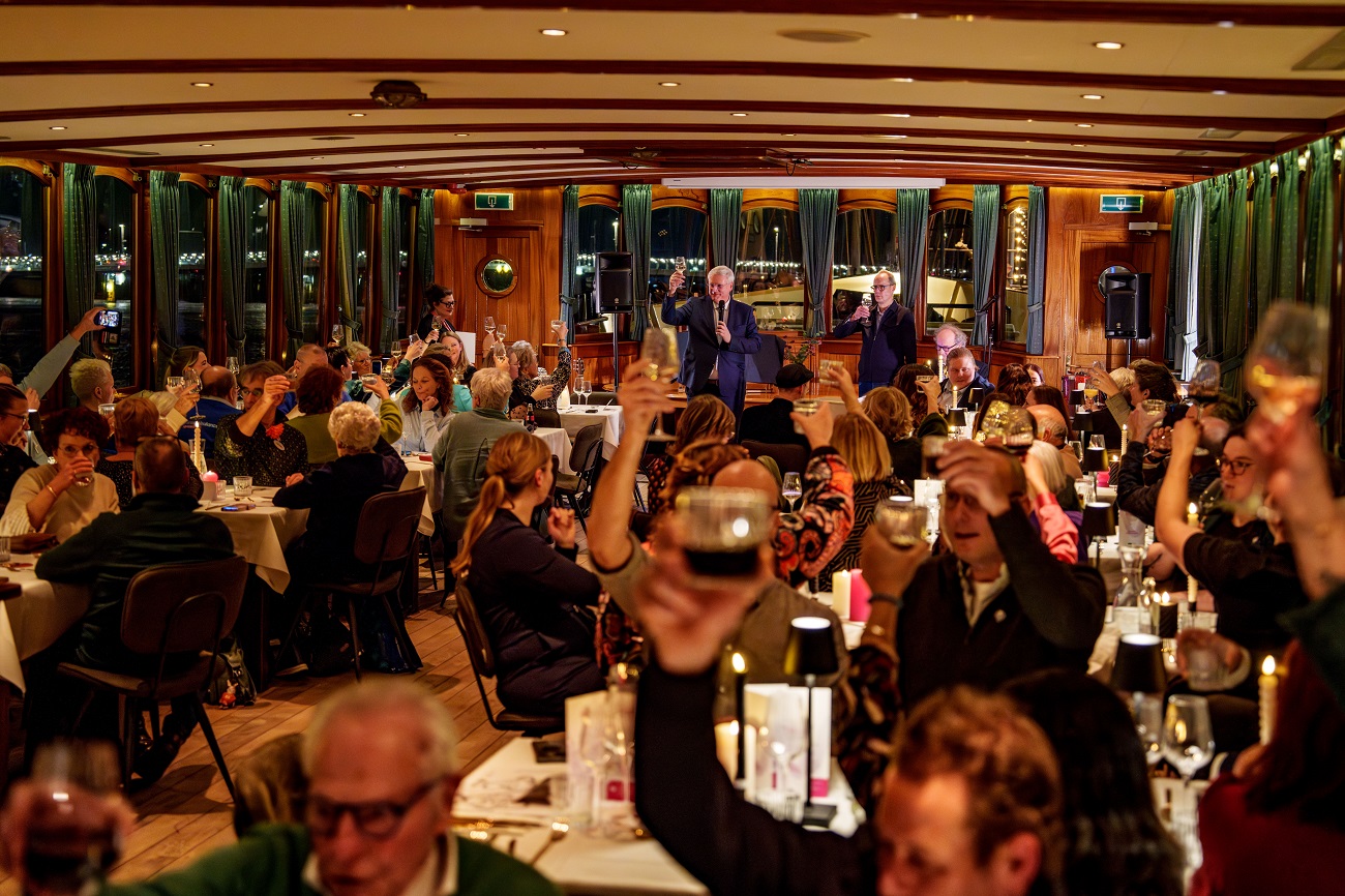 Feestzaal waarin dinertafels staan. Er is een proostmoment.