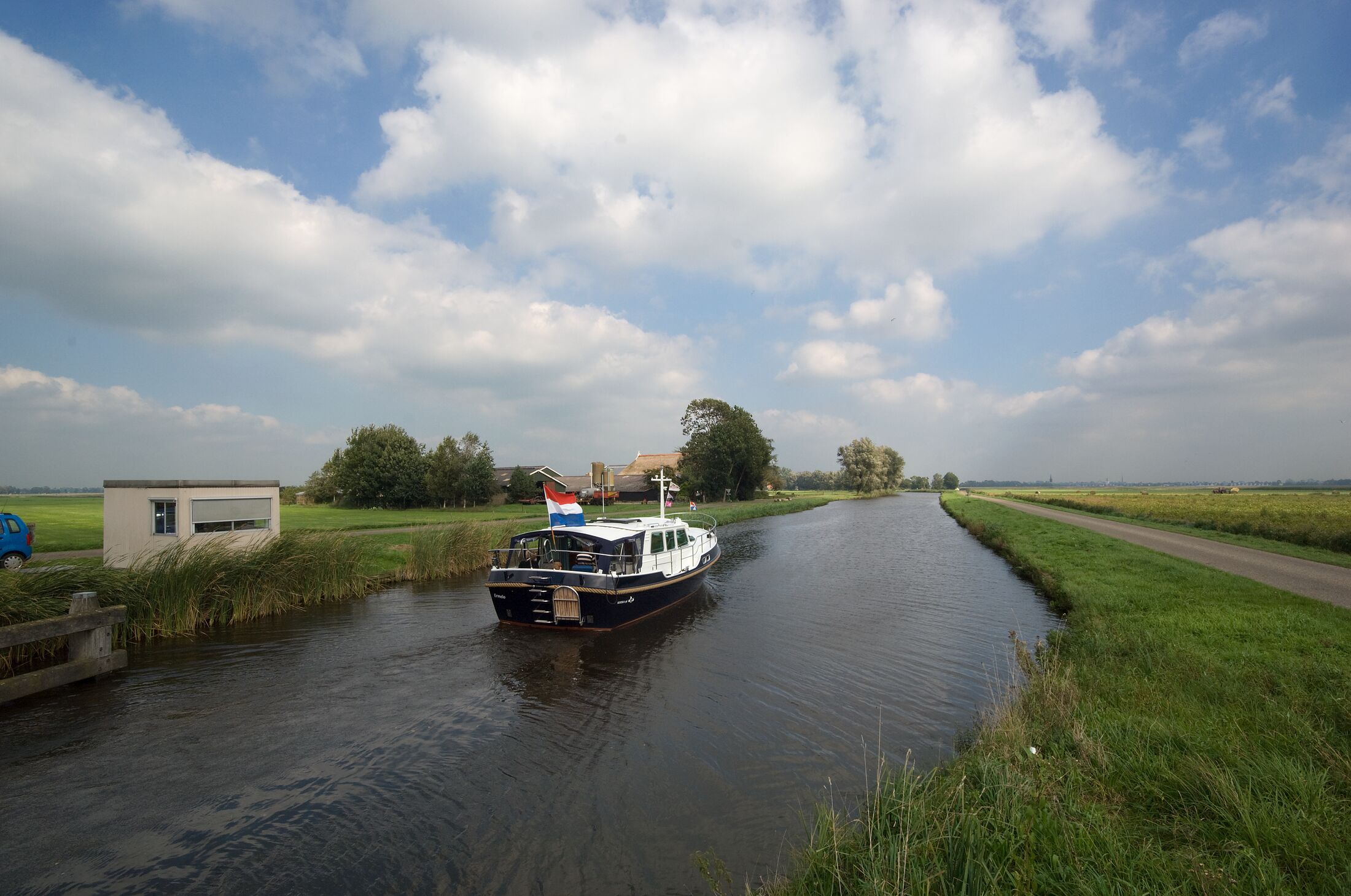 Foto van boot die vaart op sloot tussen landschap en weg