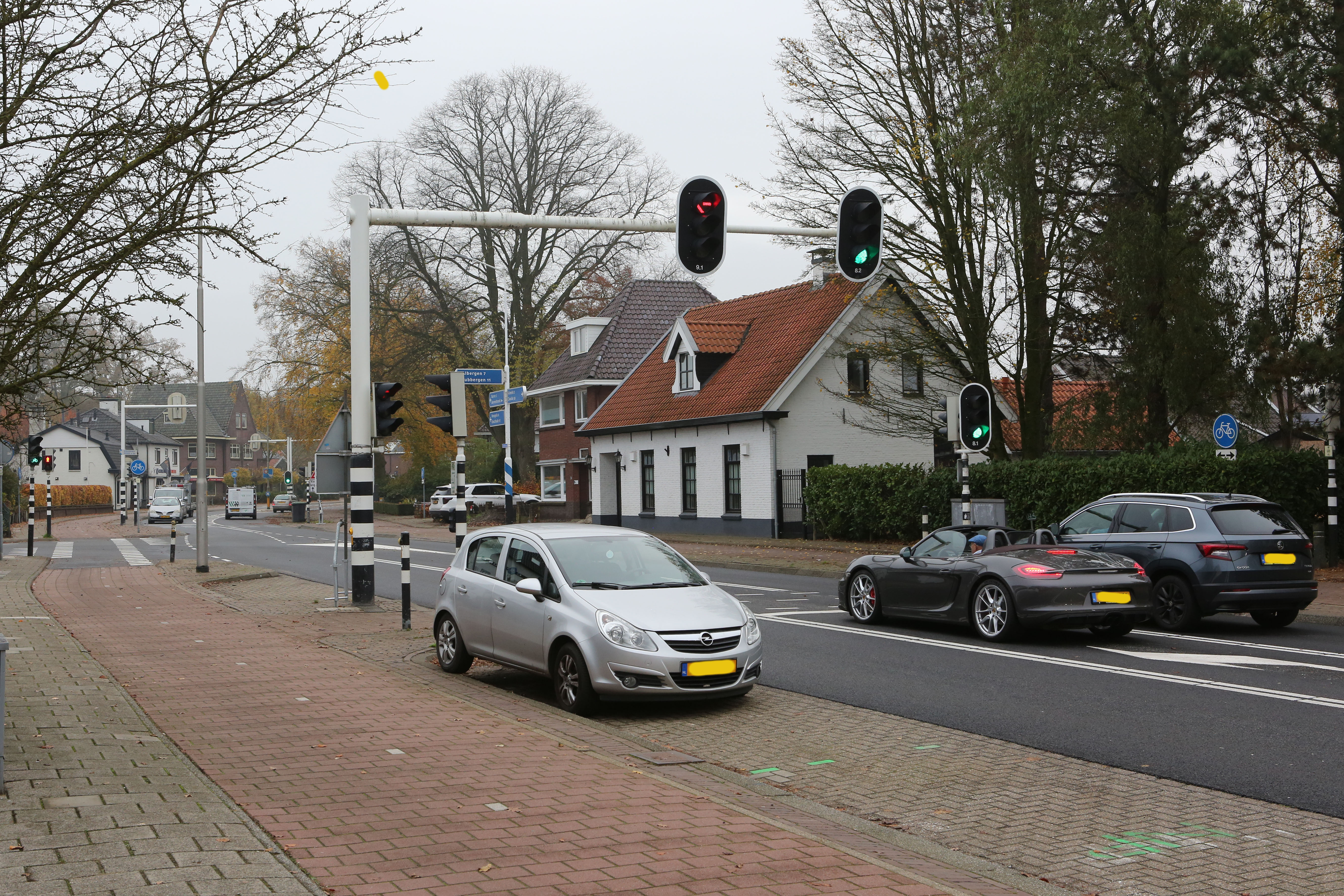 Vloedbelt 26 geparkeerde auto en verschillende auto's staan voor de stoplichten. Aan de kant staan huizen.