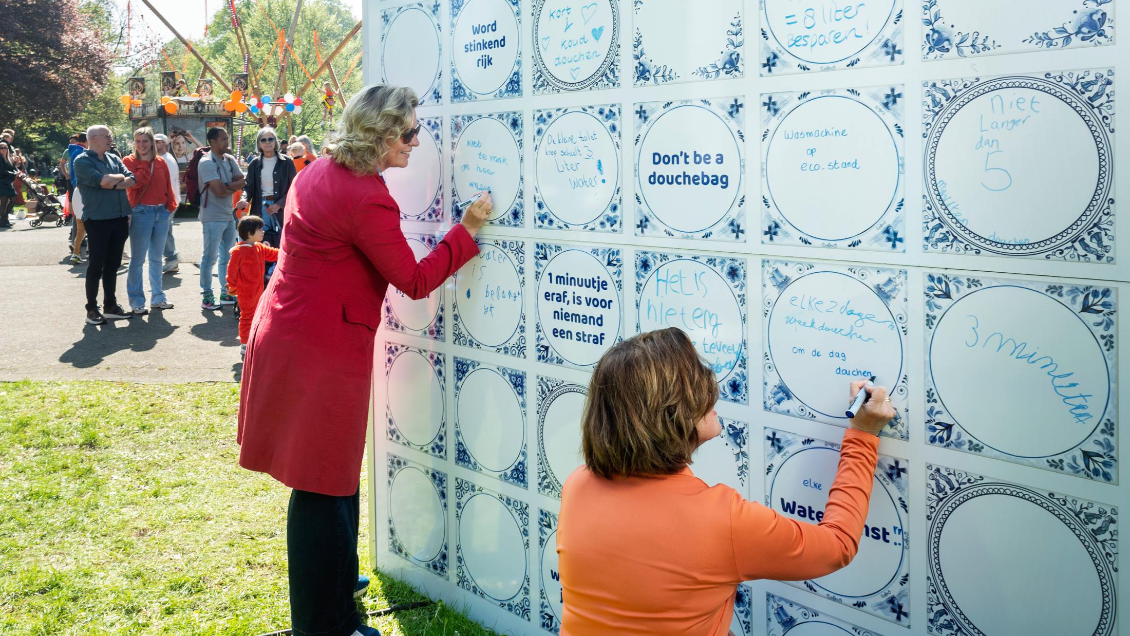 Twee vrouwen schrijven op een muur van grote, blauw-witte tegels tijdens Koningsdag 2025.