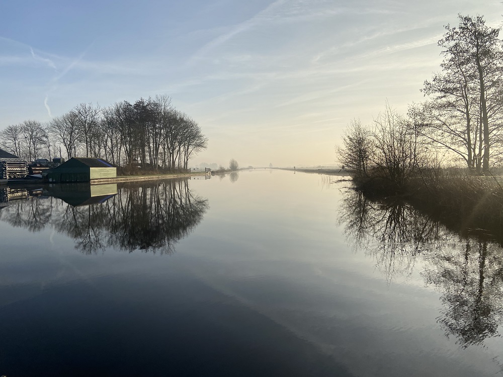 Kanaal bij het ochtendlicht met reflecterende bomen langs de rand in de winter