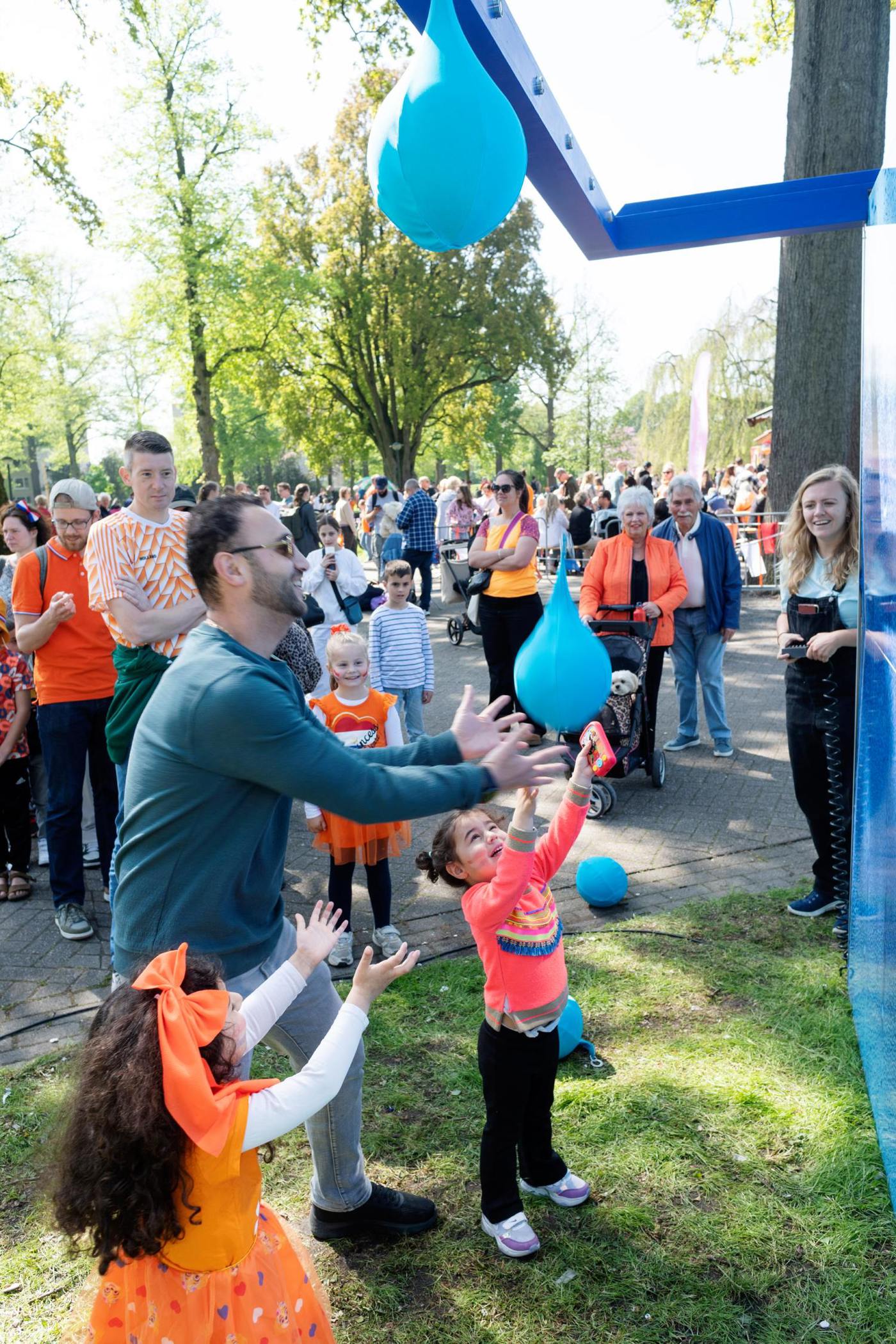 Vader en kinderen spelen enthousiast met waterballonnen bij de Vitens-stand tijdens Koningsdag 2025.