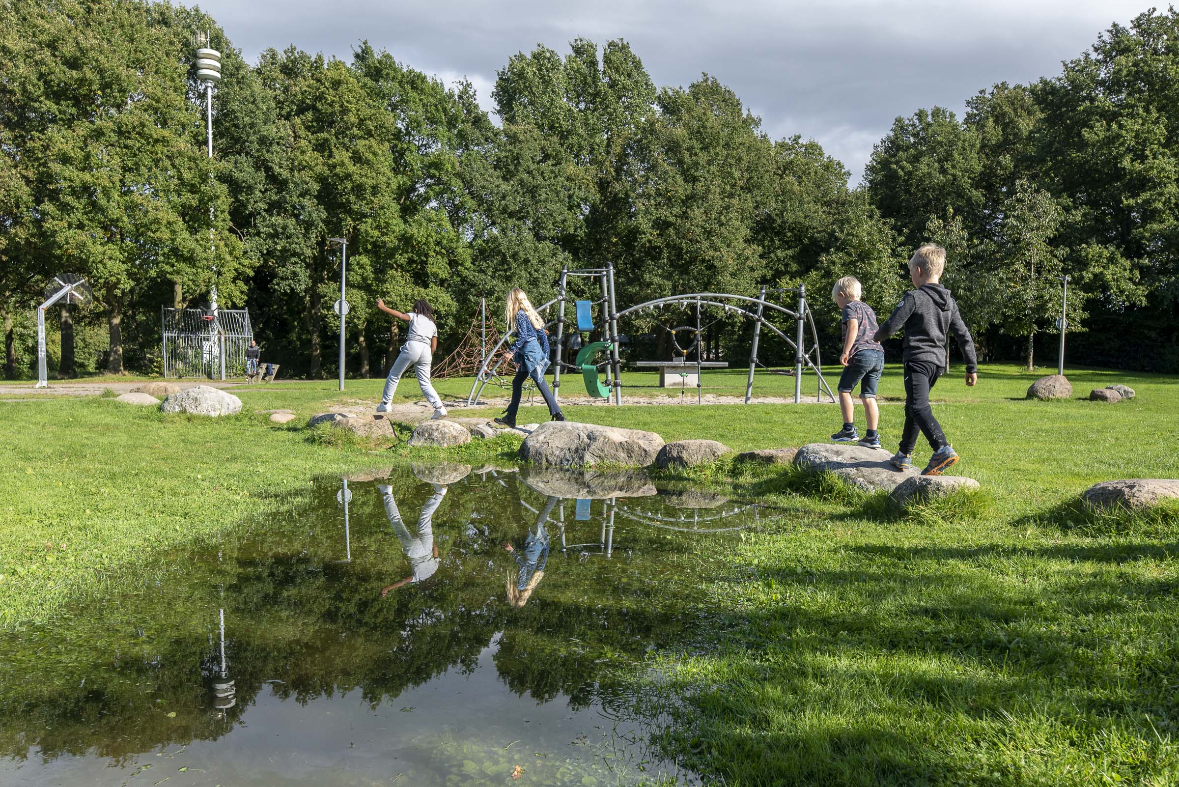 kinderen spelen in een speeltuin met veel groen en grote speelstenen