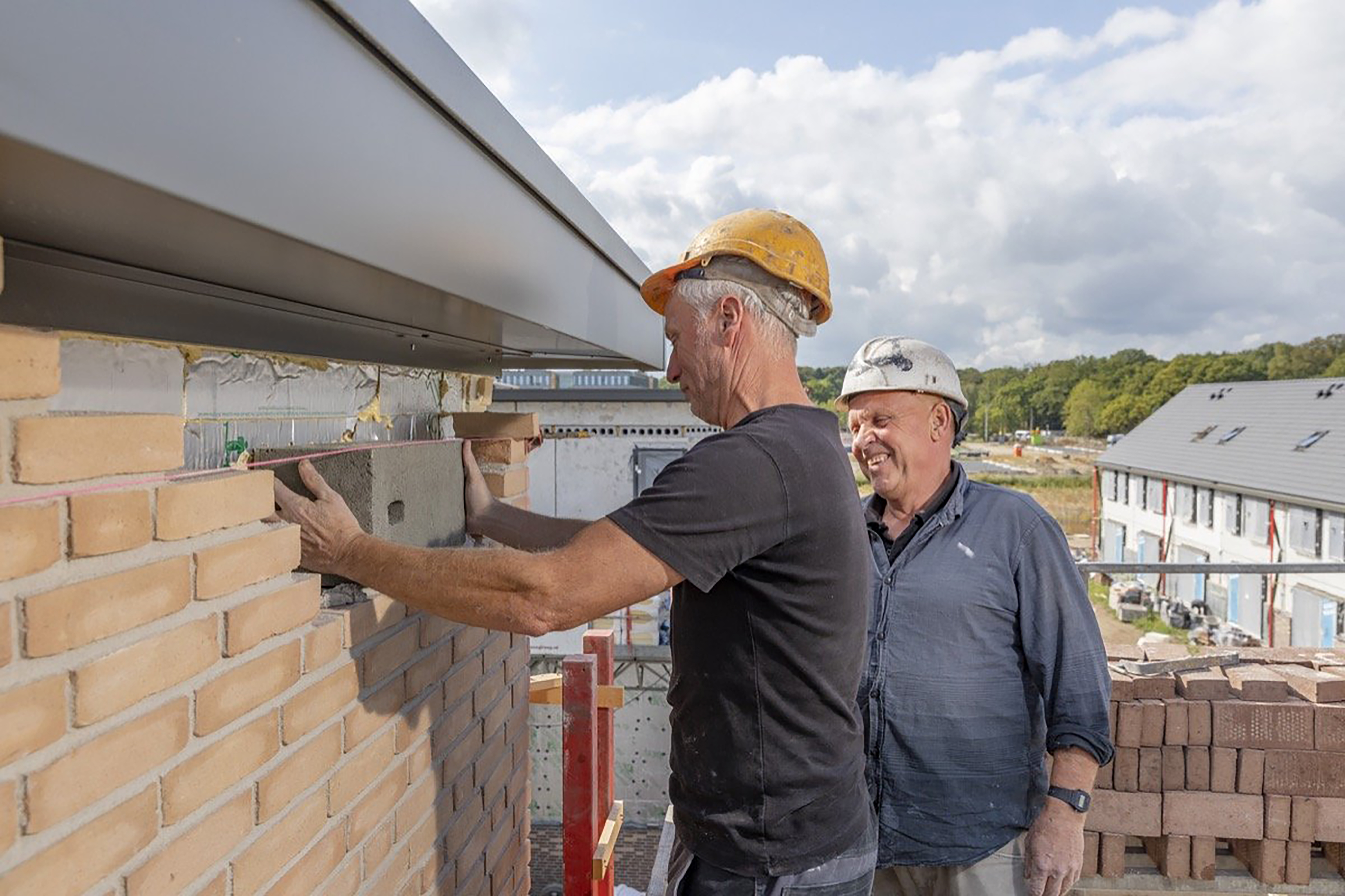 Twee mensen met witte werkhelmen zetten grijze baksteen tussen muur