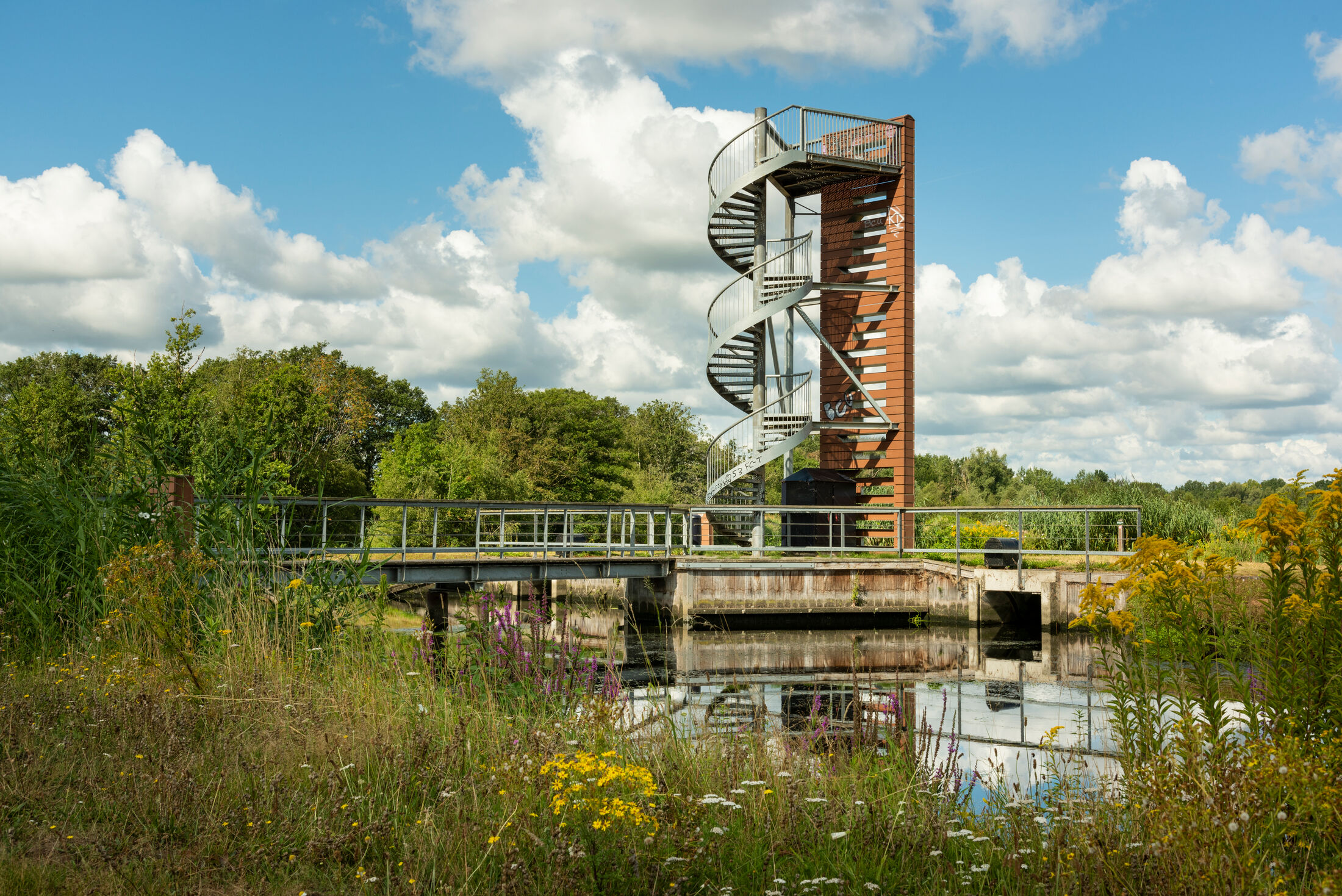 Trap naast hoge vogelspot torn naast een brug over sloot met bloemrijke overs